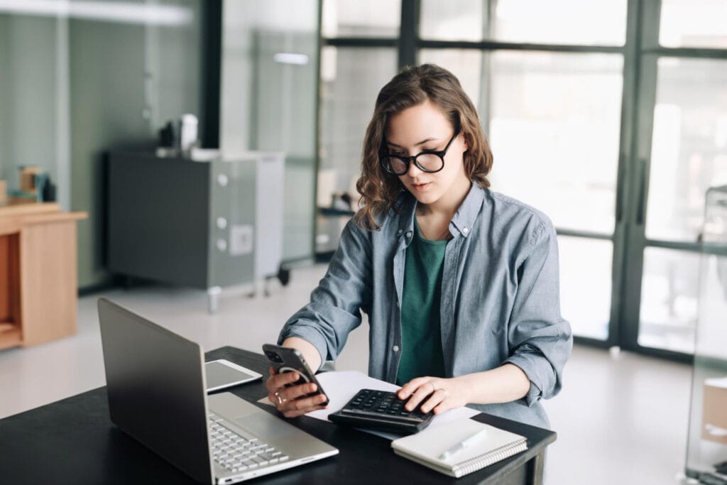 Professional woman accountant managing finances using calculator and computer in office financial