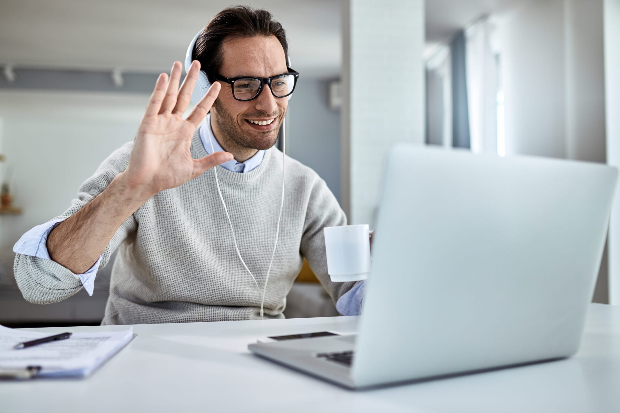 young-happy-businessman-waving-while-having-online-meeting-laptop-home